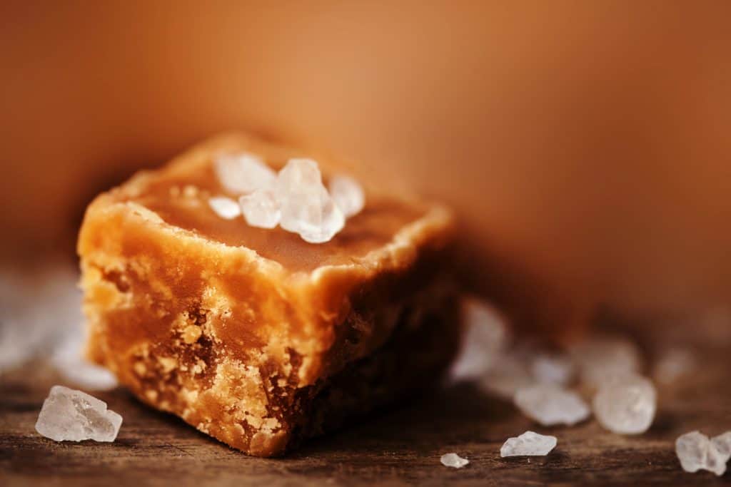 Caramel candy on brown background macro. Salted caramel piece and sea salt. Golden Butterscotch toffee caramels. Toffees.