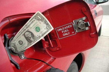 Red car with dollar bill going into gas tank, to illustrate story on saving money on gas