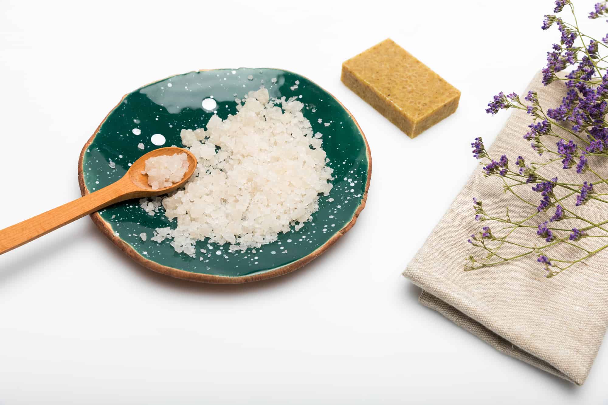 Coarse salt on a small plate with a wooden spoon next to a burlap bag of lavender for a DIY beauty treatment