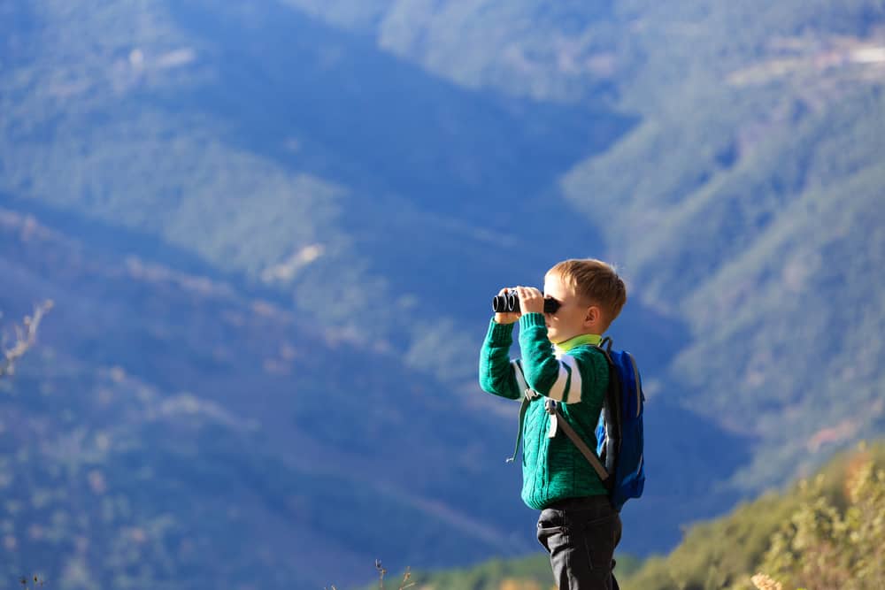 A young boy in the mountains looking through binoculars.