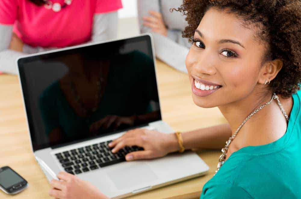 A smiling young woman in front of a laptop.