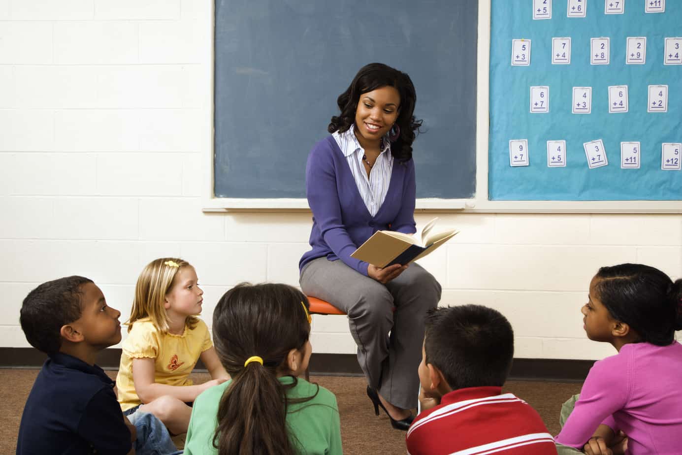 An African-American female teacher reads to elementary students.