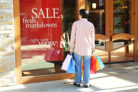 End of quarter bargains - Man with shopping bags looking at store sale sign