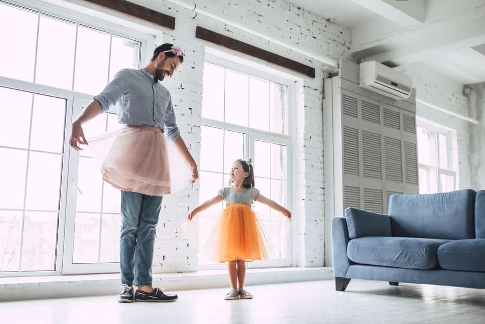 A dad in a tutu doing ballet with a little girl in living room.