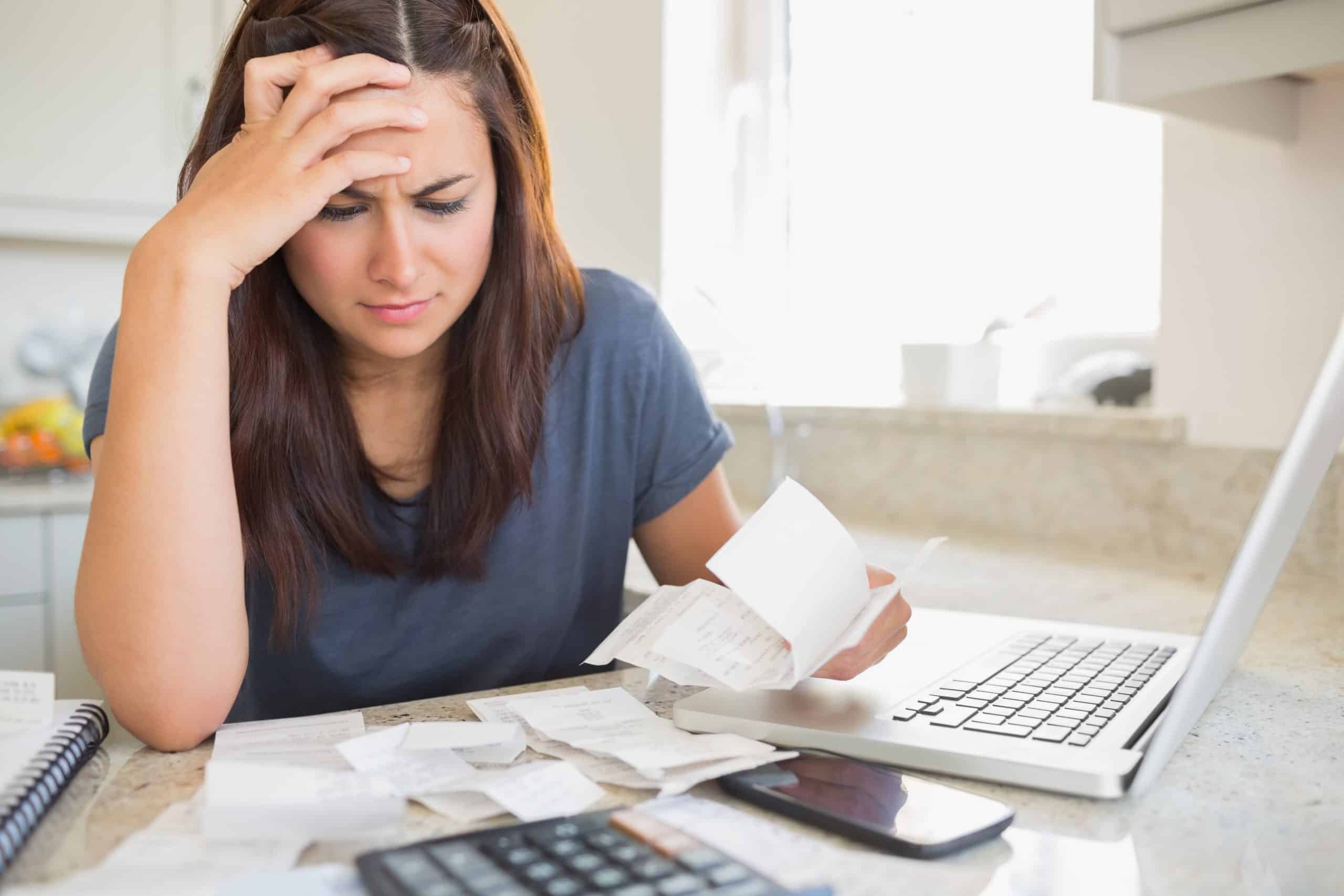 How to build an emergency fund - Brunette looking worried over bills in kitchen