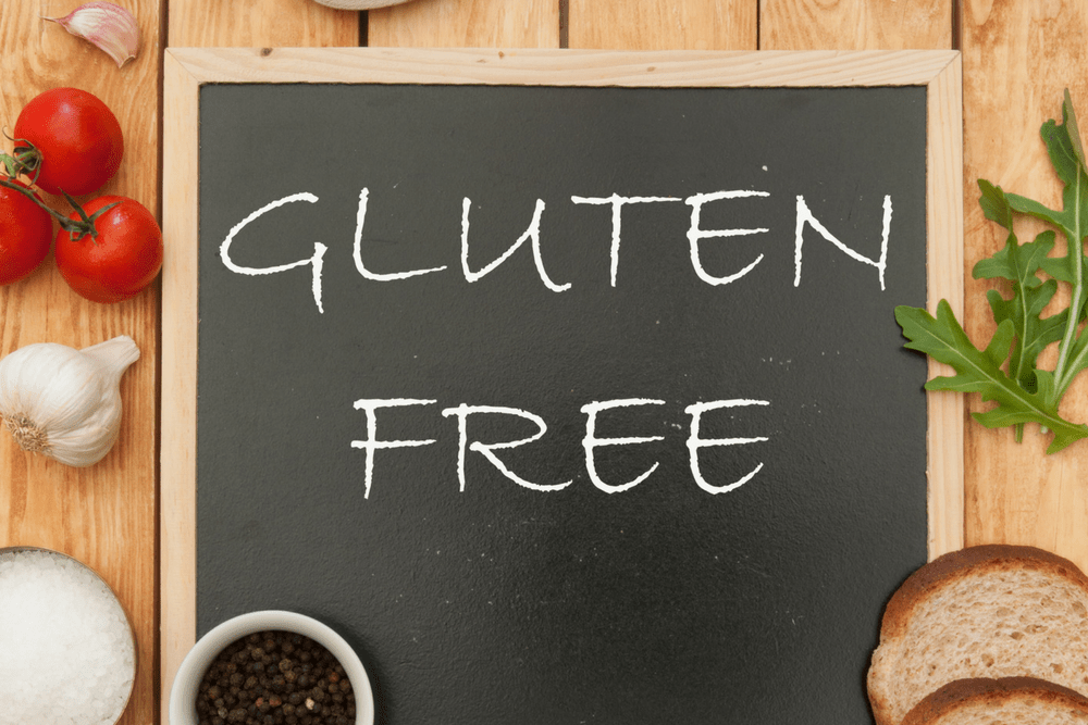 A small chalkboard with the words "Gluten Free" on it, surrounded by vegetables and bread.