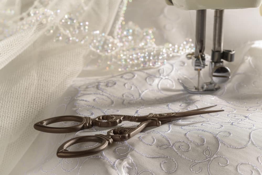 Antique scissors on wedding dress fabric next to a sewing machine.