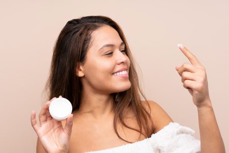 Save on skin care - Young Brazilian girl with moisturizer over isolated background