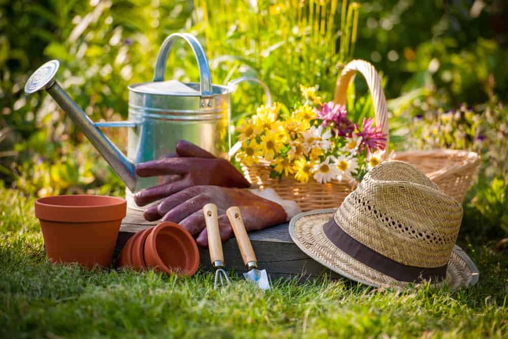 Regadera, sombrero de paja y canasta, guantes de arcilla y herramientas de jardín