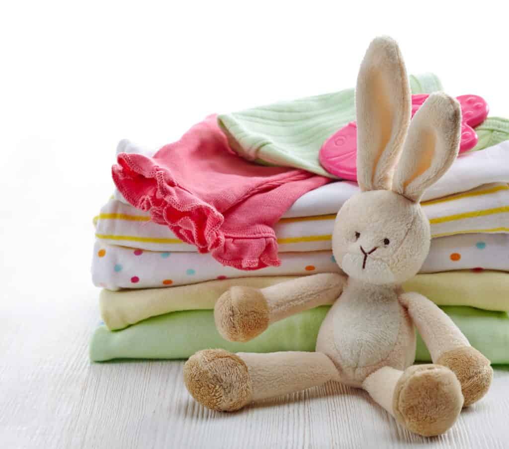 A stack of baby clothes and burp cloths with a small stuffed bunny toy