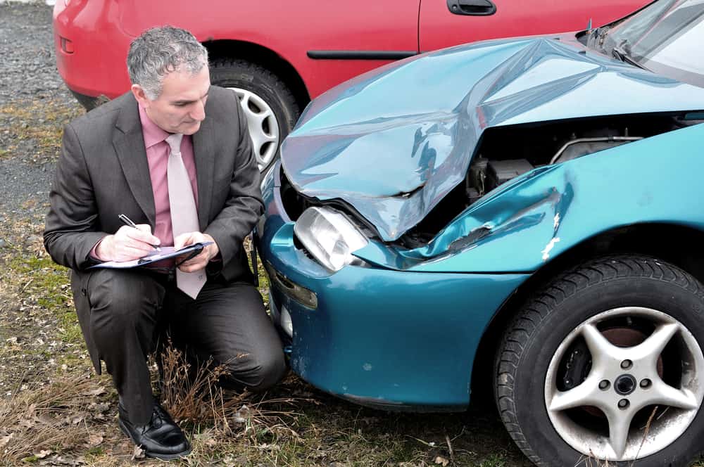 Man in suit writing down details about front end of car that has been in a collision
