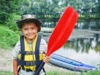 happy boy holding paddle near kayak at summer camp