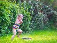 Cheap DIY water toys - Funny laughing little girl in a colorful swimming suit running though garden sprinkler playing with water splashes having fun in the backyard on a sunny hot summer vacation day