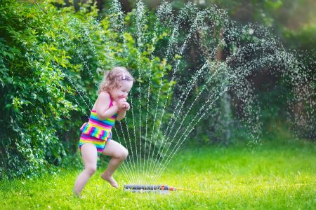 Cheap DIY water toys - Funny laughing little girl in a colorful swimming suit running though garden sprinkler playing with water splashes having fun in the backyard on a sunny hot summer vacation day
