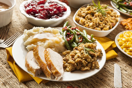 A plate with turkey, green beans and dressing, surrounded by a bowl of cranberry sauce and other traditional Thanksgiving side dishes.