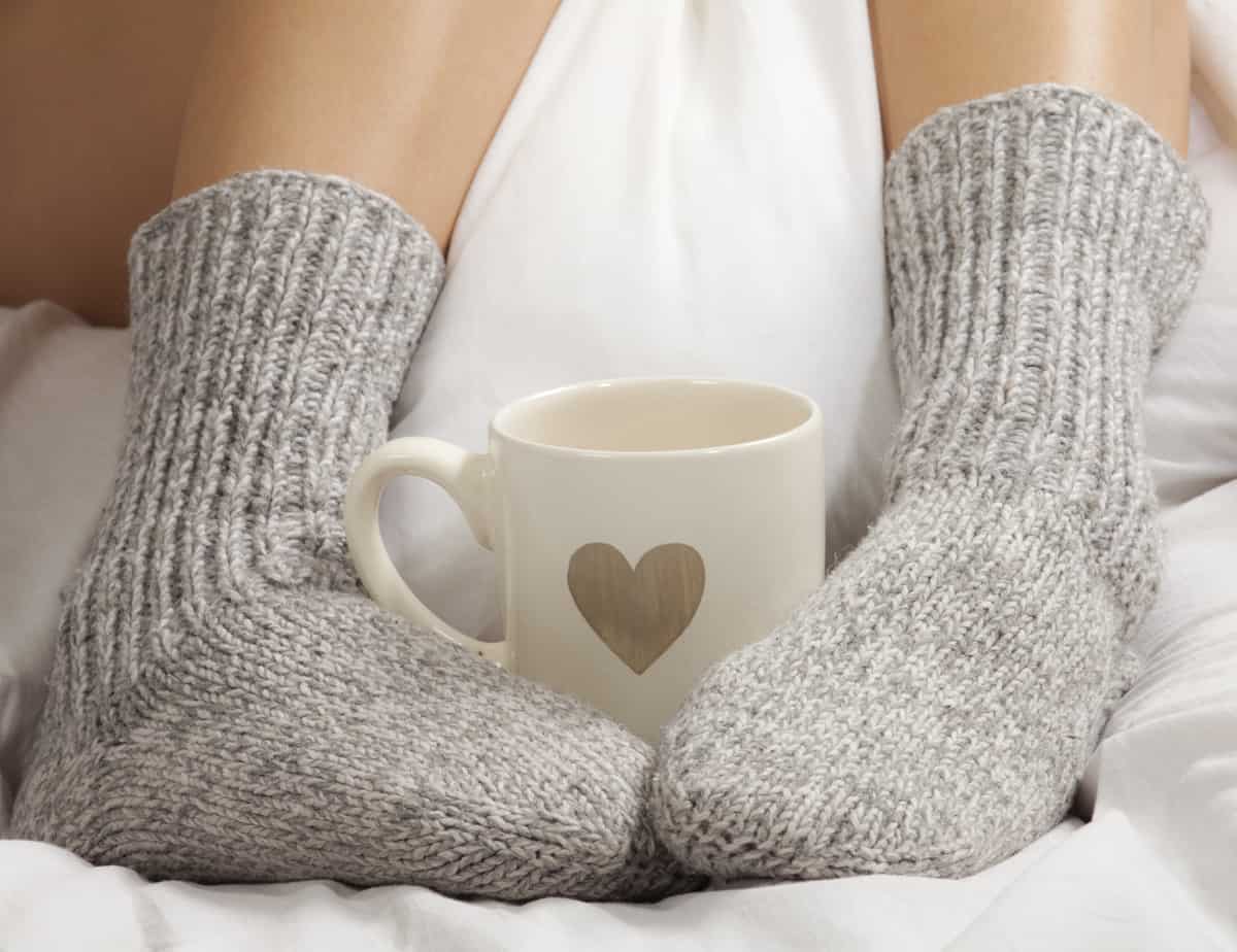 Closeup of person's feet with warm socks and mug in the middle.