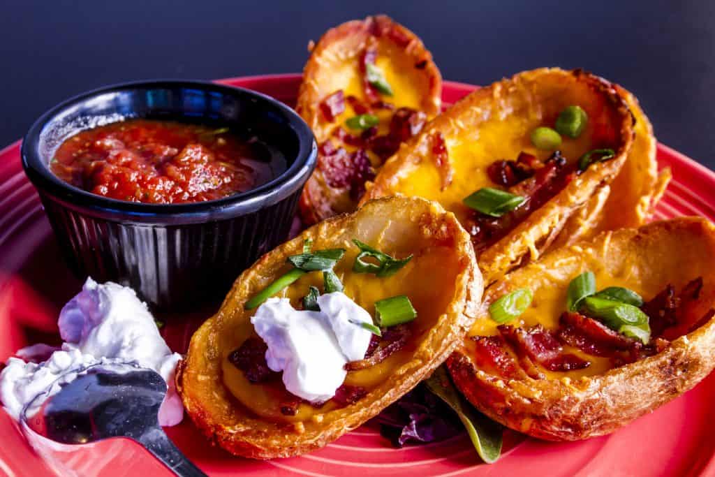 Potato skins filled with melted cheddar cheese, bacon and onion chives topped with sour cream 