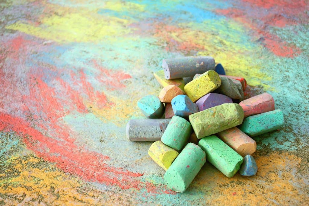 A pile of sidewalk chalk on a rainbow colored background.