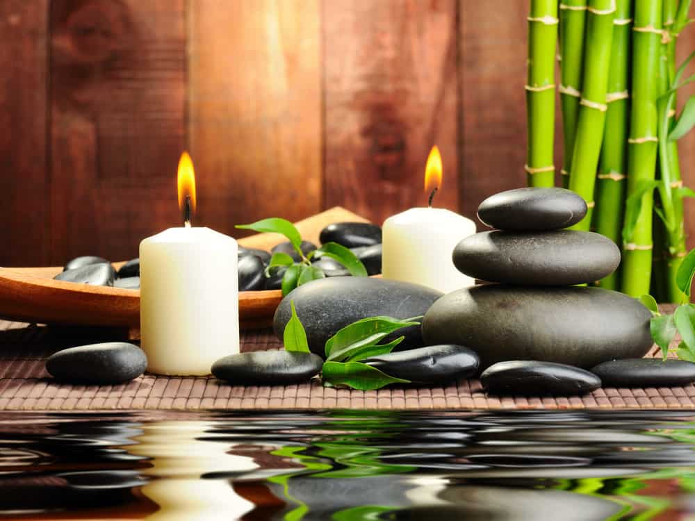 Candles and stacks of river rocks reflected in water with bamboo in background.
