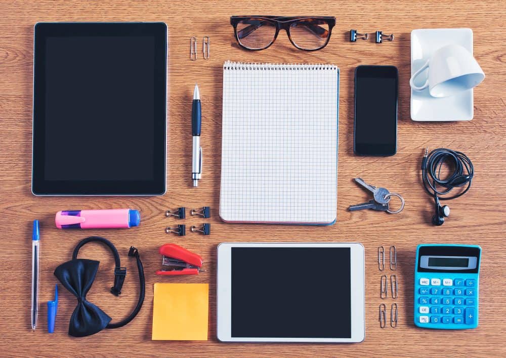 An assortment of items like eyeglasses, a pen, a tablet computer, a notebook and a calculator scattered on a desktop.