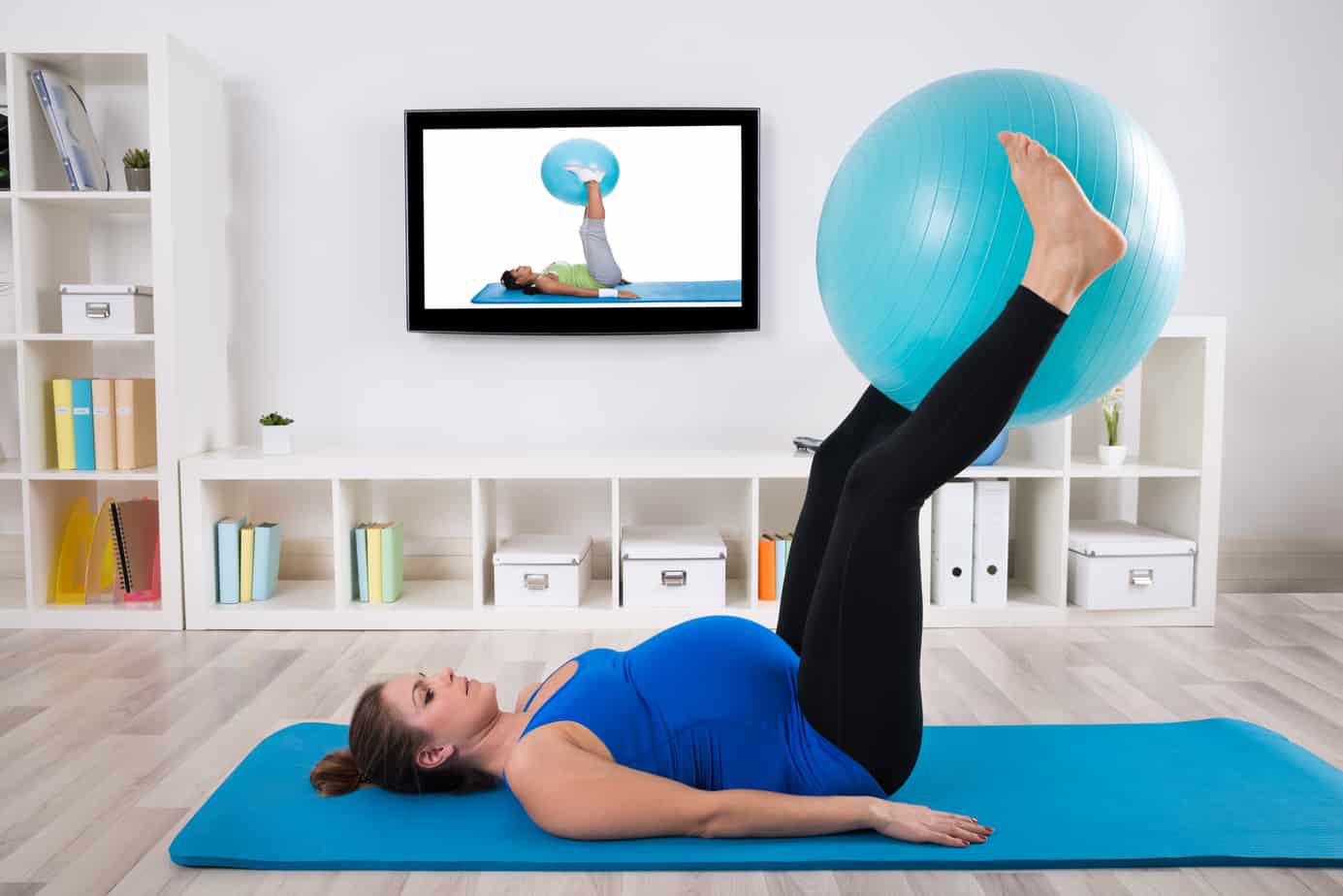 Pregnant woman exercising with exercise ball in living room.