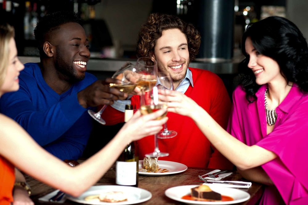 Four young adults toasting each other in restaurant.