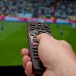 tv coverage of live sports with a hand holding a remote control in front of the screen