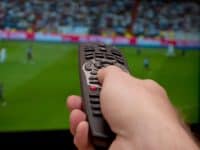 tv coverage of live sports with a hand holding a remote control in front of the screen