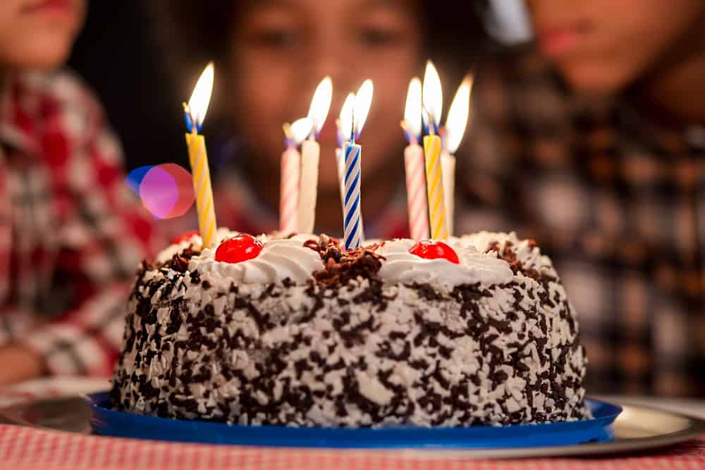 A small chocolate birthday cake with candles with a girl in the background.