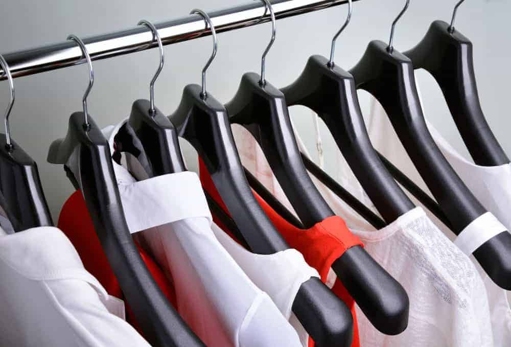 White blouses hanging on black hangers with a few red tops in between them.