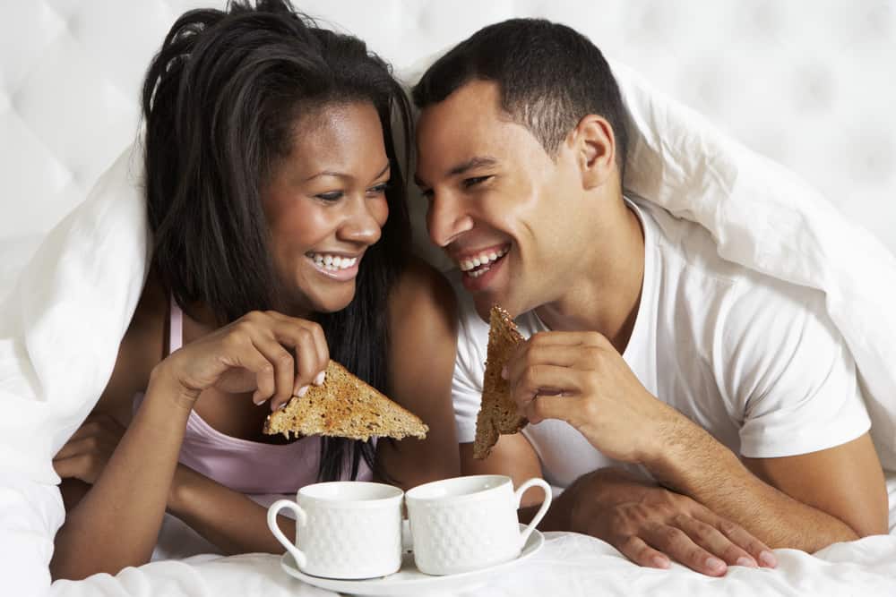 A couple eating breakfast in bed with toast and coffee.