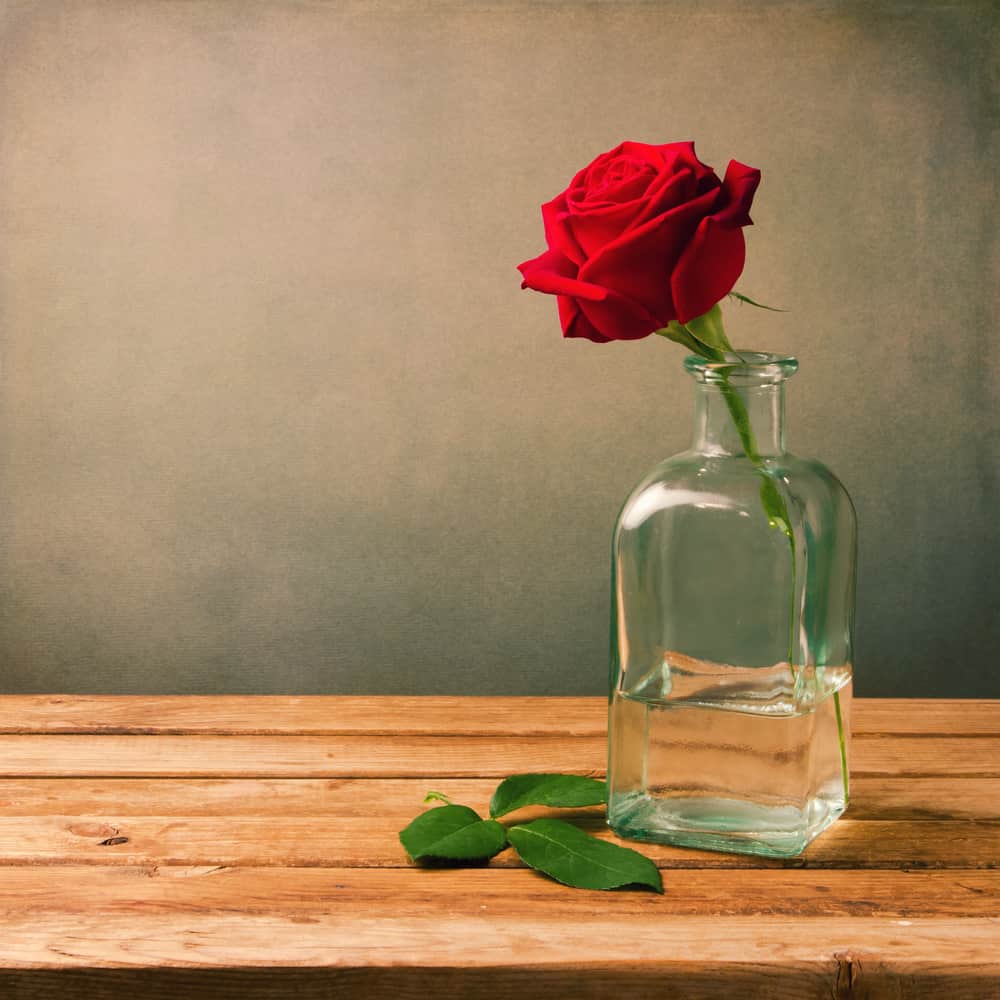 A single red rose in a vase on a wooden table.
