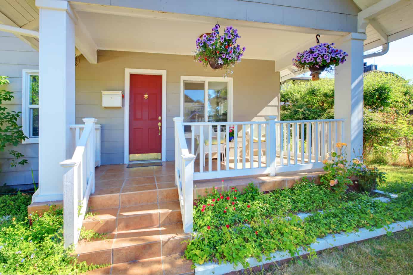 A front porch with a white railing and flower baskets leading to a red door.