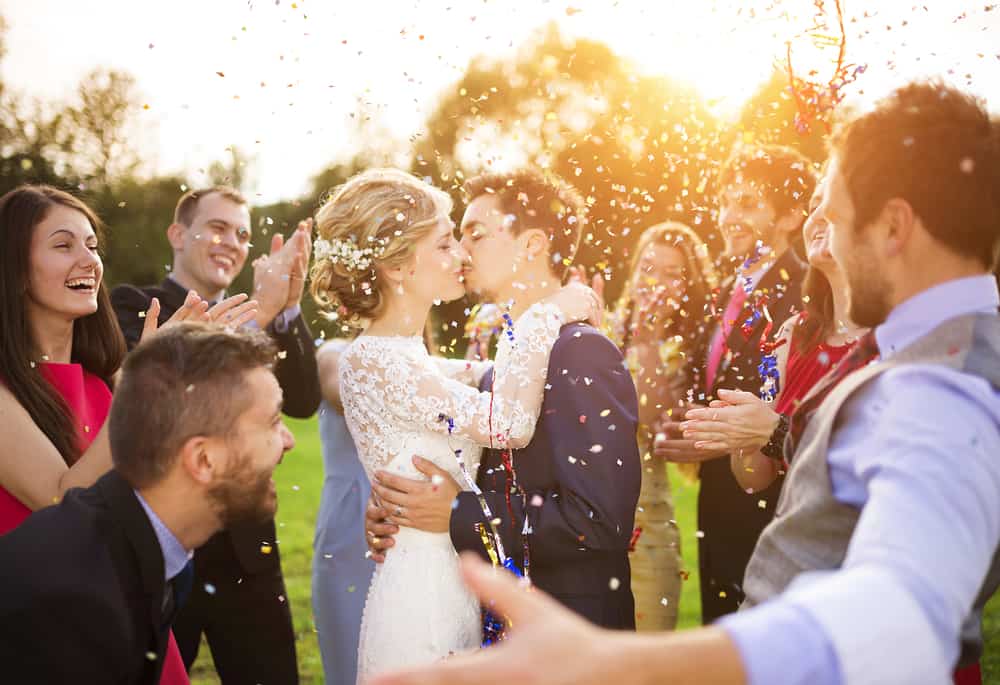 Bride and groom kissing at outdoor ceremony surrounded by friends.