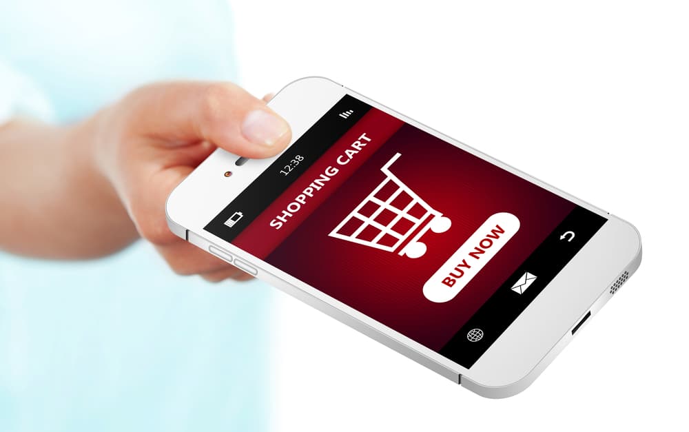 Hand holding mobile phone with shopping cart on screen with "Buy Now"