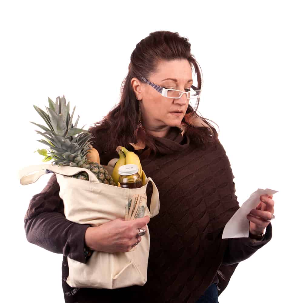 A woman holding a bag of groceries checking her receipt.