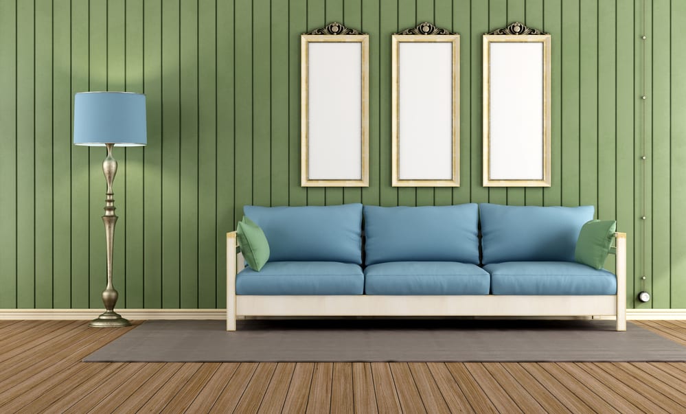 A blue midcentury modern couch against a wall with wood paneling painted green.