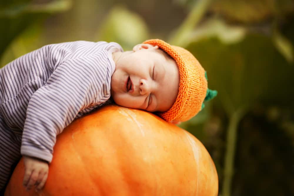 Sleeping baby with pumpkin hat slumped over on top of pumpkin.