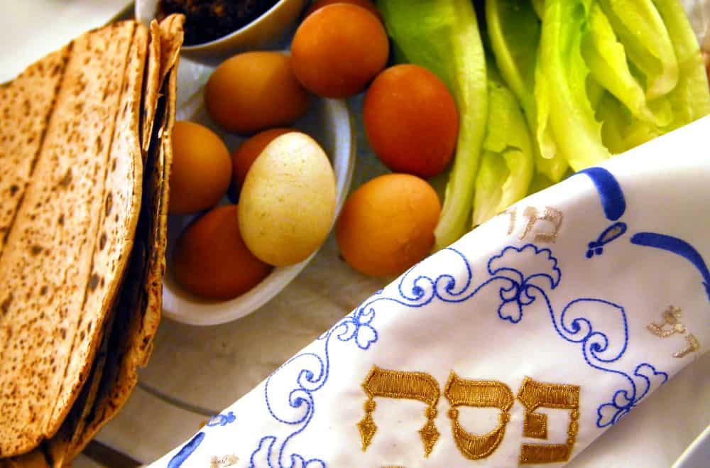 A closeup of a Passover table including matzo, hard-boiled eggs and bitter herbs.