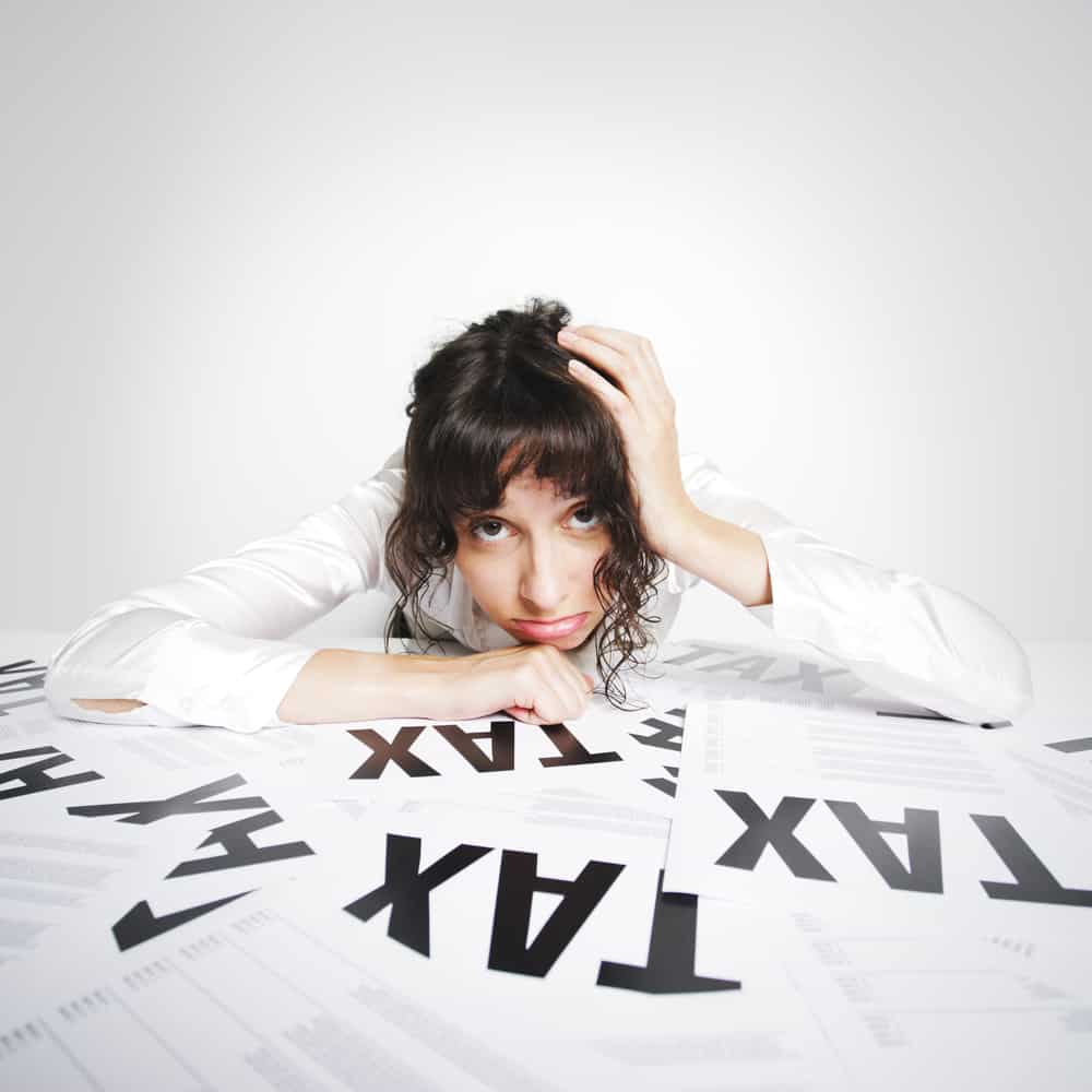 Illustration of frustrated woman slumped over papers that say "TAX"