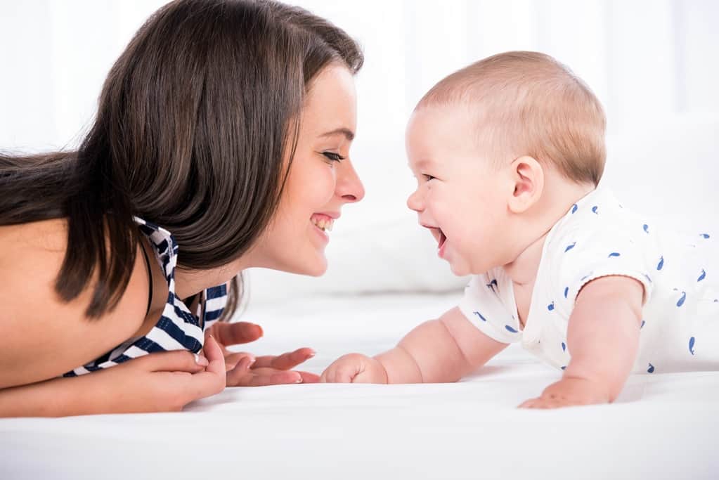 Mom and baby on floor smiling at each other.
