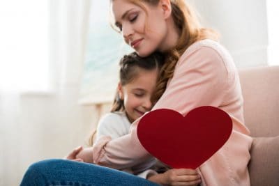Mother and daughter embrace with homemade heart card