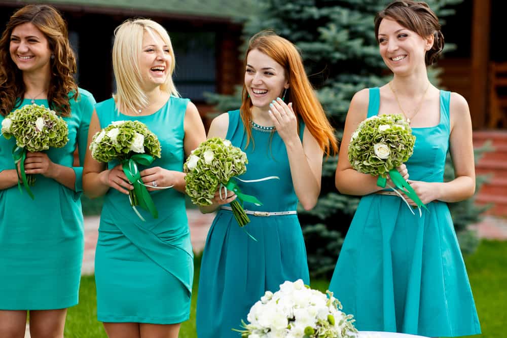 Four bridesmaids in teal dresses holding bouquets.