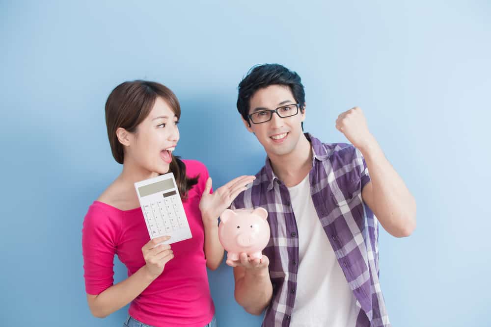 Young woman holding calculator and young man holding piggy bank, both smiliing.