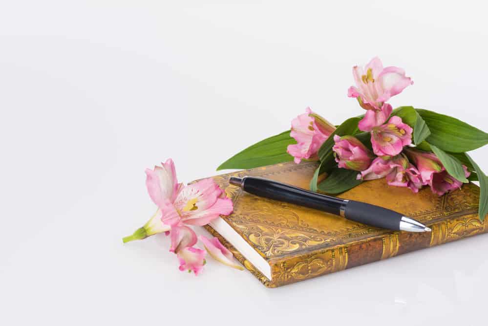 A gold journal with pink flowers and a pen on top of it.