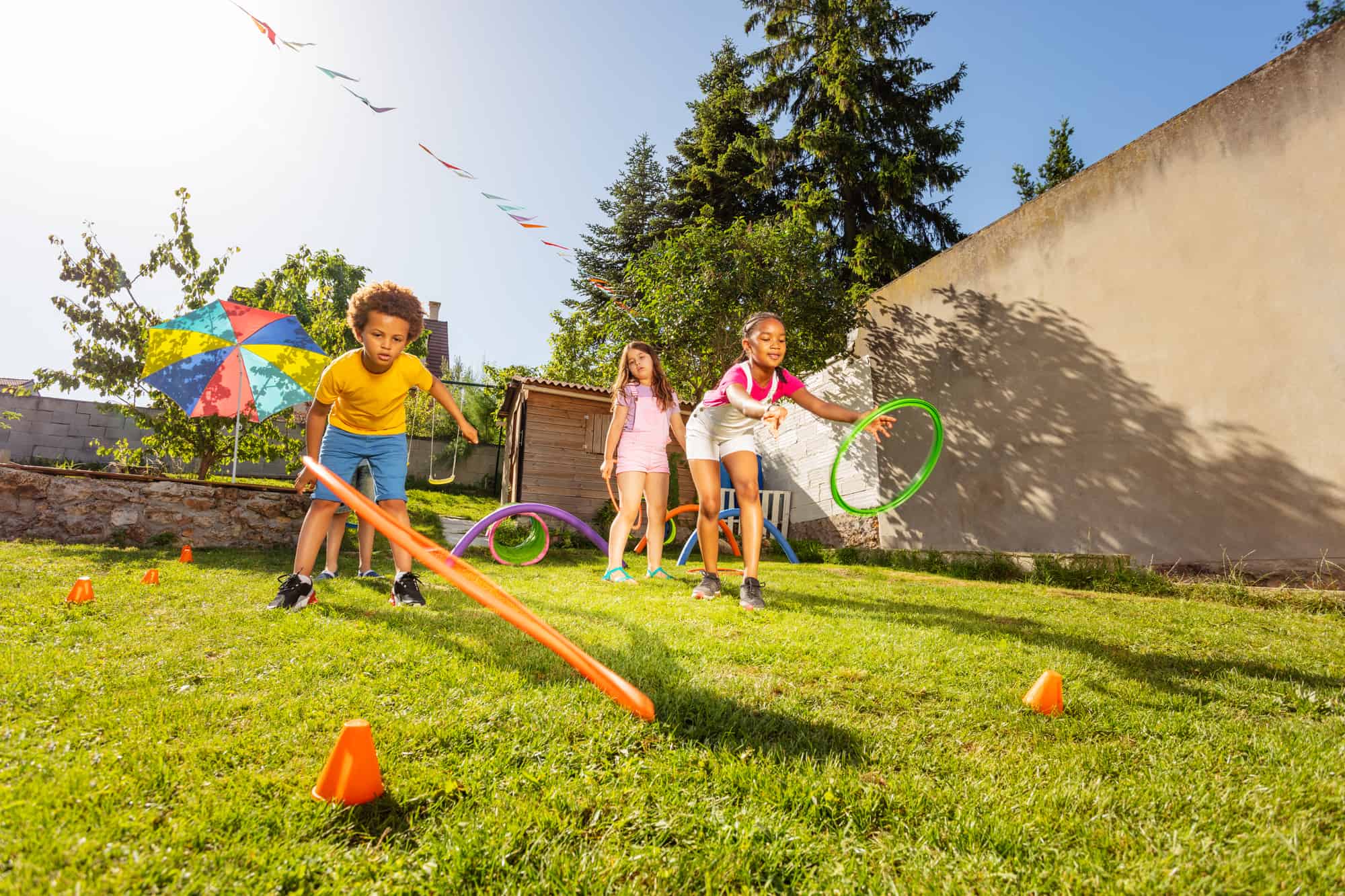 Group of diverse kids throwing circles, sports hoops to the target playing game on the lawn