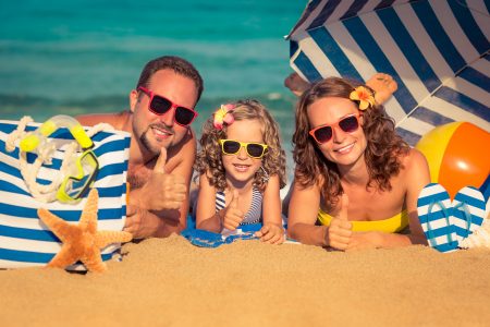 How to save for vacation - dad, girl and mom lying on the beach giving the thumbs up sign