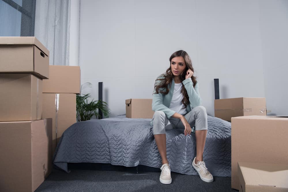 Young woman sitting on bed surrounded by moving boxes