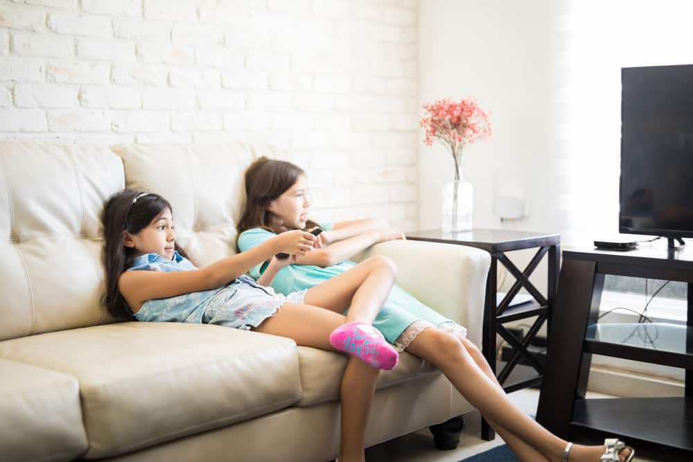 Two young girls watching TV on a couch.