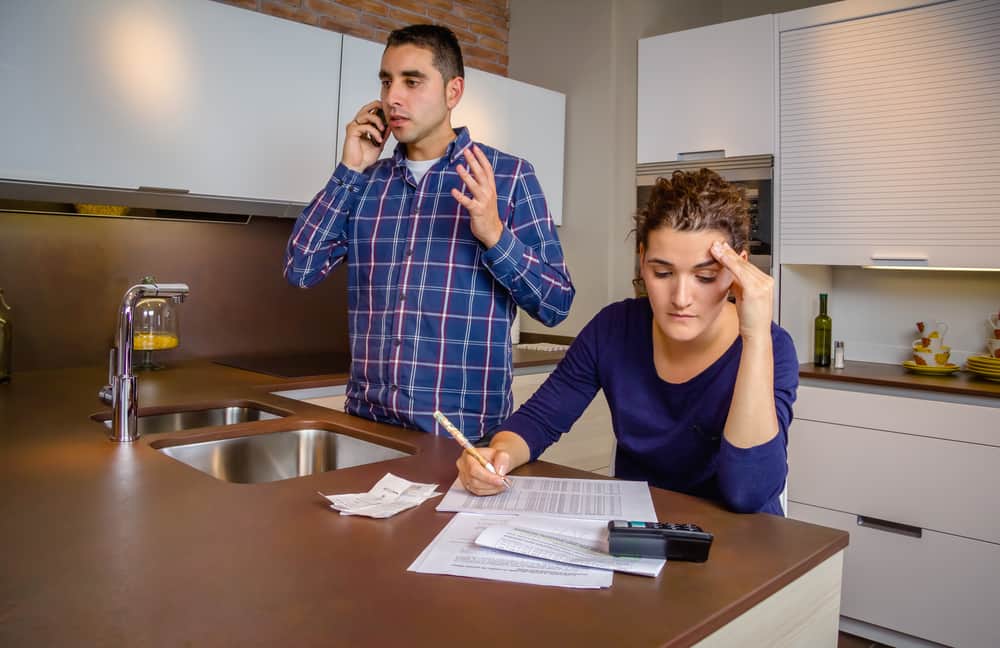 Man on phone while woman looks at stack of bills with pencil in hand